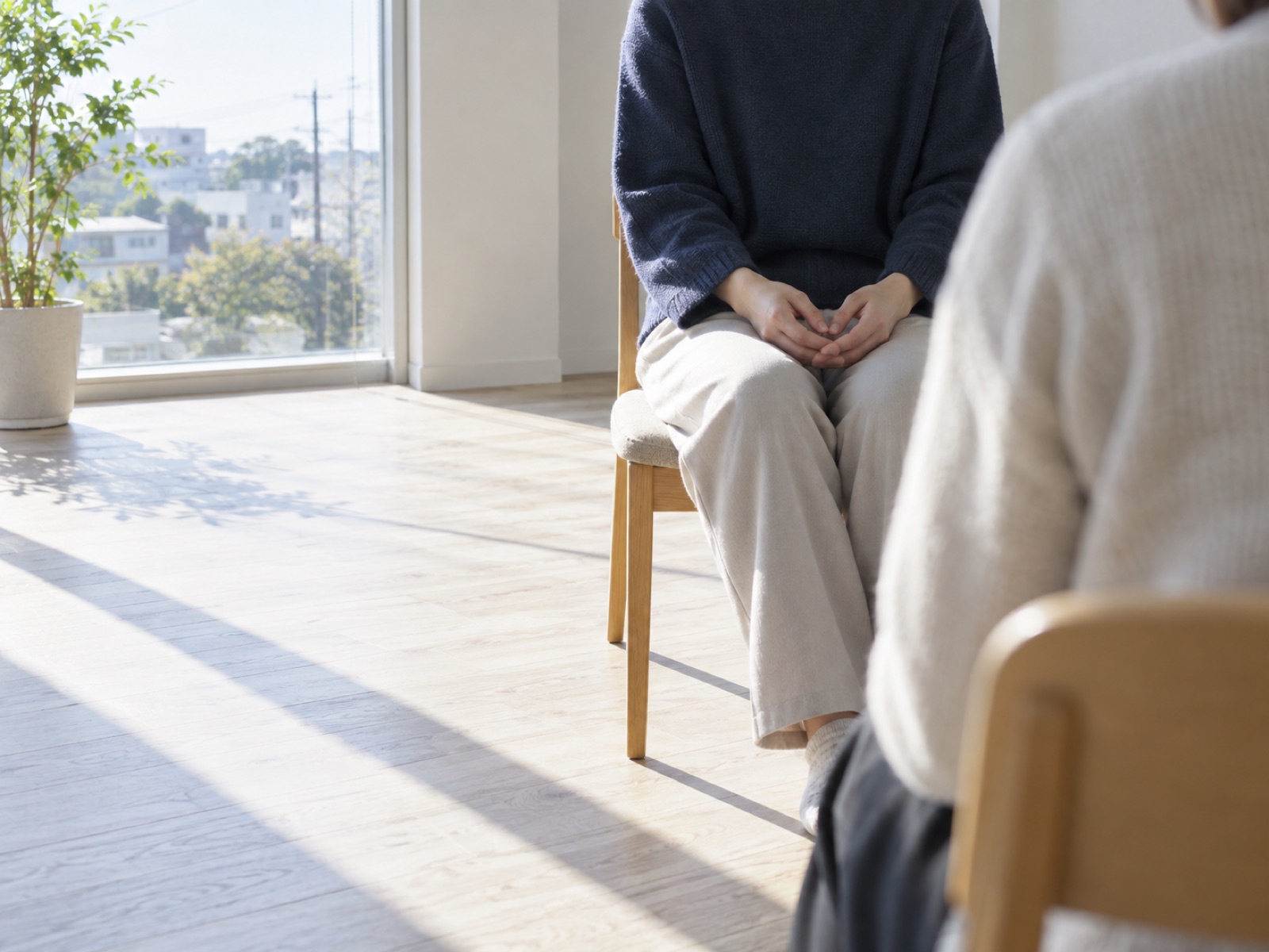 窓辺で向かい合う2脚の椅子と、膝の上で組まれた手